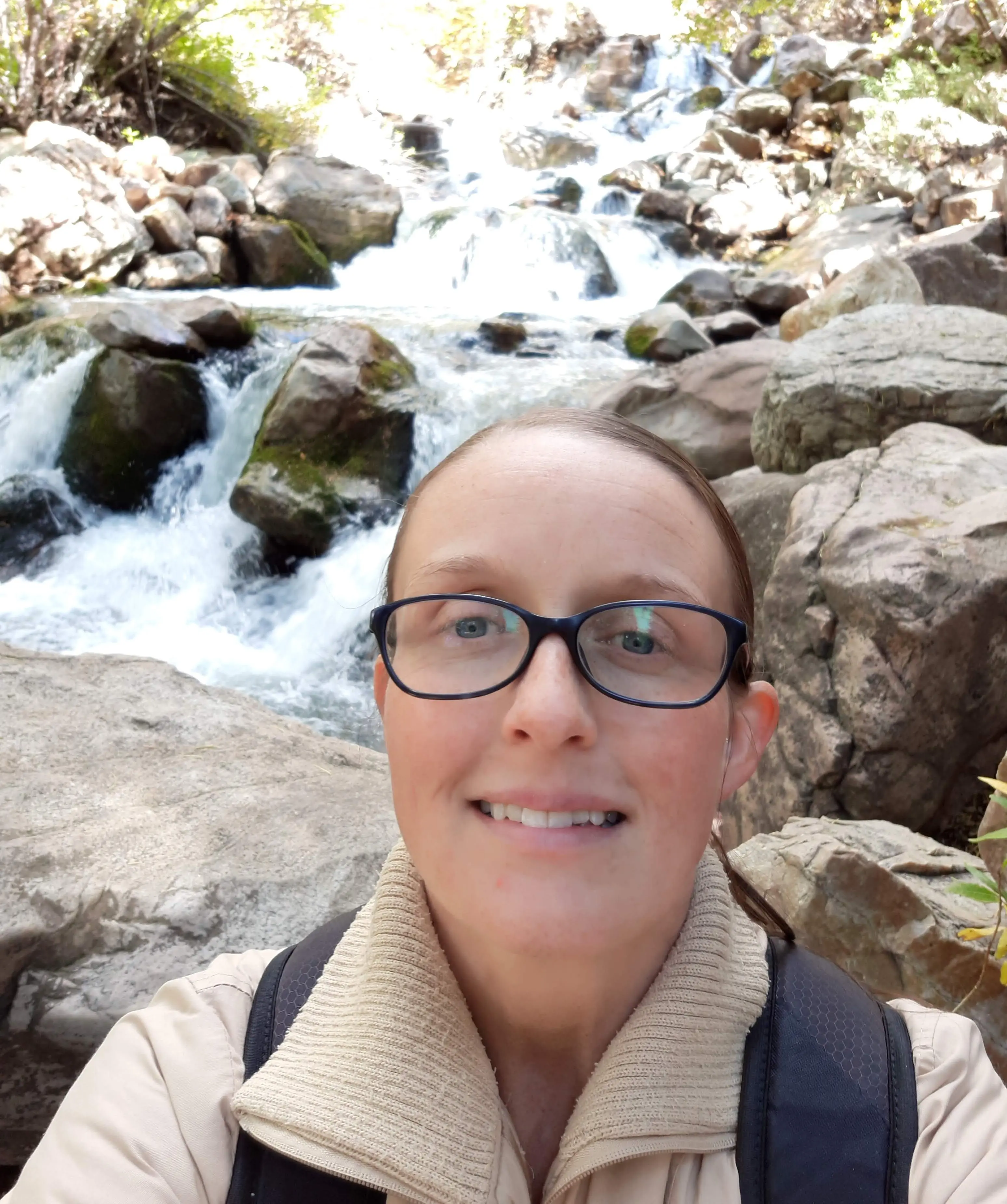 a woman with glasses standing in front of a stream.