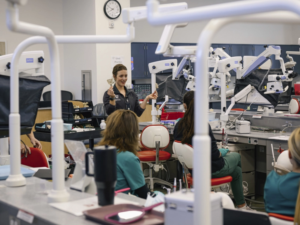A woman giving instruction to students in a dental lab classroom.