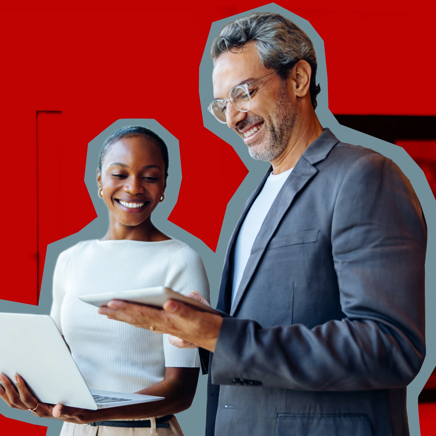 A man smiling and looking at a tablet next to a woman holding a laptop computer.